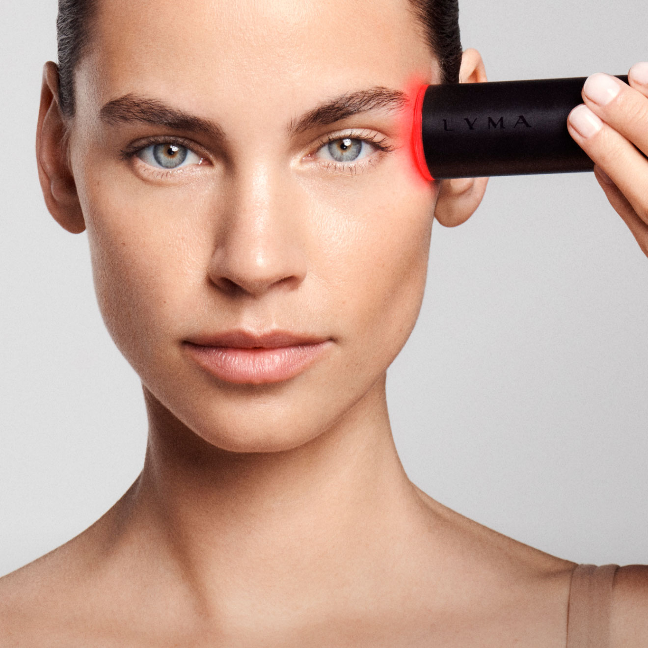 Mujer joven usando el lyma laser rojo en el rostro. el lyma tiene un cuerpo negro y una luz roja